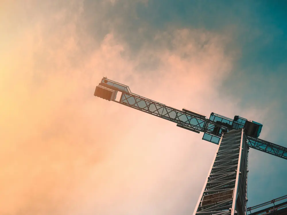 Grue de chantier vue en contre-plongée sur un ciel orangé, devant un immeuble en construction