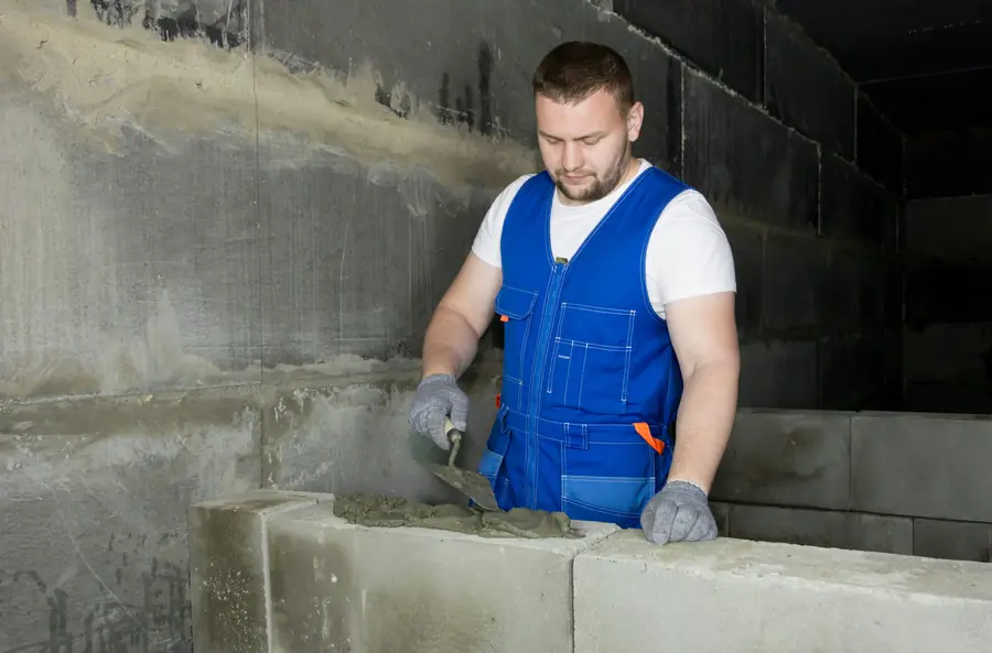 Maçon étalant le mortier à la truelle sur un mur en blocs béton